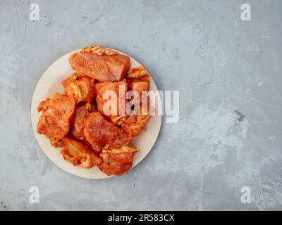 Roher truthahn in einer Marinade mit Gewürzen auf einem freundlichen Einwegteller. Mariniertes Hähnchen zum Grillen und grillen. Rohes gewürztes Fleisch für Shish Kebab auf Grau Stockfoto