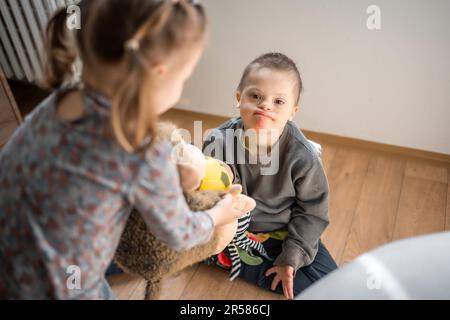 Boy mit Down-Syndrom und ASD spielt mit seiner jüngeren Schwester im Schlafzimmer Stockfoto