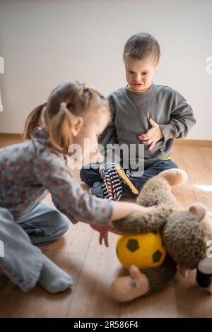 Boy mit Down-Syndrom und ASD spielt mit seiner jüngeren Schwester im Schlafzimmer Stockfoto