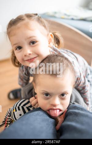 Boy mit Down-Syndrom und ASD spielt mit seiner jüngeren Schwester im Schlafzimmer Stockfoto