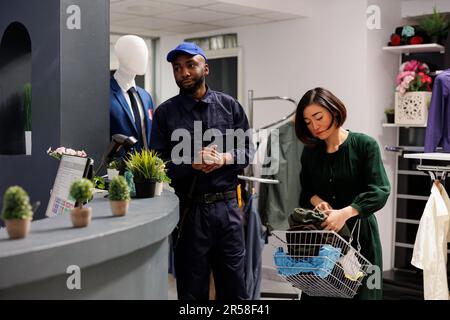 Junger afroamerikanischer Sicherheitsbeauftragter im Einzelhandel in Uniform steht am Kasse des Bekleidungsgeschäfts, sorgt für die Sicherheit von Mitarbeitern und Kunden, patrouilliert im Bekleidungsgeschäft Stockfoto