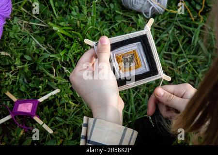 Ein Mädchen macht indische Amulette-Mandalas „Ojos de dios“ (Gottes Augen) in einem Park Stockfoto