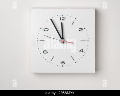 Eine Wanduhr isoliert auf weißem Hintergrund. Es ist fünf vor zwölf. Stockfoto