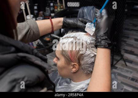 Nahaufnahme der Hände eines Friseurs, der Kopf, Haare und Wurzeln des Kunden mit einer Bürste in einem Friseursalon malt. Stockfoto