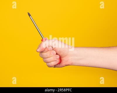 Hand mit einem Schraubenzieher. Kein Gesicht, gelber Hintergrund. Stockfoto