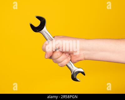 Eine Hand hält einen Maulschlüssel. Kein Gesicht, gelber Hintergrund. Stockfoto