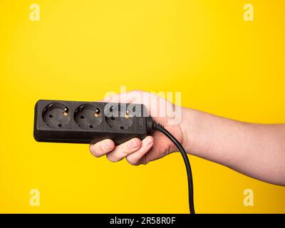 Eine Hand hält eine Steckdosenleiste. Kein Gesicht, gelber Hintergrund. Stockfoto