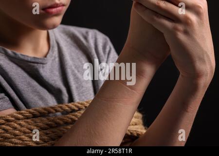 Ein kleiner Junge gefesselt und als Geisel genommen, auf dunklem Hintergrund, Nahaufnahme Stockfoto