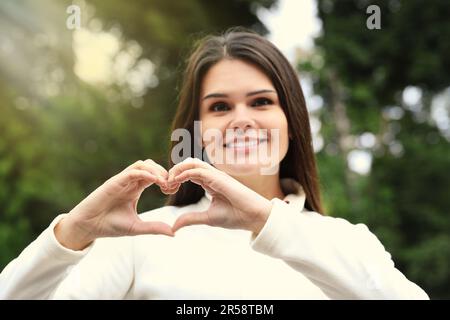 Fröhliche junge Frau, die sich mit den Händen im Freien ein Herz bildet Stockfoto