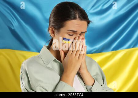 Traurige junge Frau mit gefalteten Händen nahe der ukrainischen Flagge Stockfoto