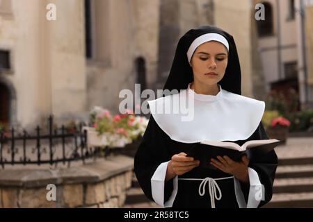 Junge Nonne, die Bibel in der Nähe von Gebäuden im Freien liest, Platz für Text Stockfoto