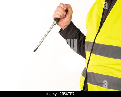 Ein Arbeiter in einer Sicherheitsweste hält einen großen Schraubenzieher in der Hand. Kein Gesicht, gelber Hintergrund, Kopierraum. Stockfoto