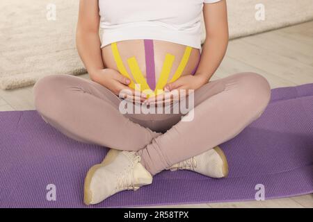 Schwangere Frau mit Kinesio-Videos, die im Haus Yoga-Matte macht, Nahaufnahme Stockfoto