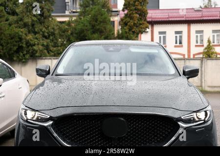 Schwarzes Auto mit eingeschalteten Scheinwerfern in Wassertropfen im Freien Stockfoto