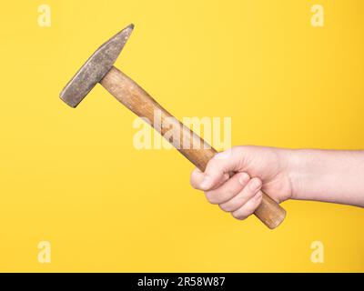 Eine Hand hält einen Hammer vor einem gelben Hintergrund. Kein Gesicht, Kopierraum, Konzept. Stockfoto