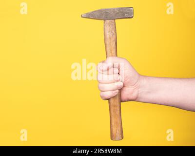 Eine Hand hält einen Hammer vor einem gelben Hintergrund. Kein Gesicht, Kopierraum, Konzept. Stockfoto