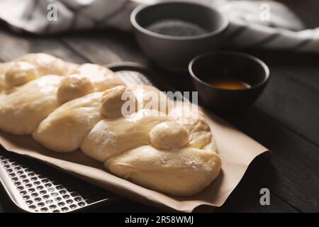 Rohes geflochtenes Brot und Zutaten auf schwarzem Holztisch, Nahaufnahme. Traditionelle Sabbat-Challah Stockfoto