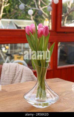 Pinkfarbene Tulpen in Glasvase auf Holztisch auf der Terrasse Stockfoto