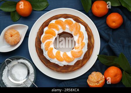 Hausgemachter Joghurtkuchen mit Tangerinen, Creme und grünen Blättern auf blauem Holztisch, flach liegend Stockfoto