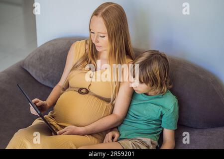 Schwangere mutter und Sohn sehen sich die Tablette an. Ein Buch lesen, einen Cartoon ansehen oder einen Videoanruf tätigen. Sehen Sie sich das Foto vom Ultraschall an Stockfoto