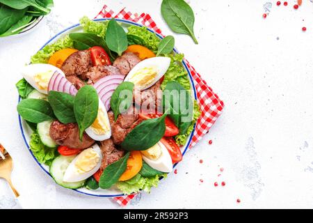 Perigord-Salat mit gerösteter Hühnerleber, roten Tomaten, Gurken, gekochten Eiern, Salat und Spinat. Weißer Küchentisch Hintergrund, Draufsicht Stockfoto