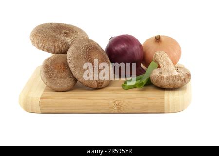 Shiitake-Pilze und verschiedene Zwiebelsorten auf einem Holzschneidbrett auf weißem Hintergrund. Rezepte und Heilkräuter Stockfoto