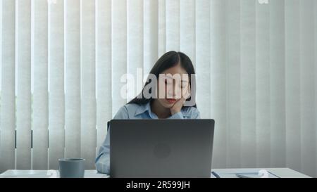 Junge asiatische Frauen sind bei der Arbeit gelangweilt und fühlen sich faul, am Nachmittag mit Daten auf ihrem Laptop umzugehen. Stockfoto