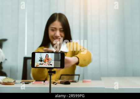 Junge asiatische Frau vloggt sich über Beauty-Produkte mit einem Video für ihren Blog über Kosmetik mit Handy-Kamera zu Hause machen. Stockfoto