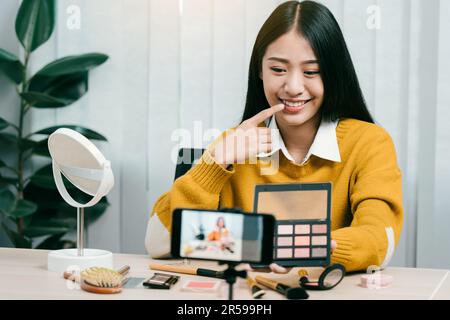 Junge asiatische Frau vloggt sich über Beauty-Produkte mit einem Video für ihren Blog über Kosmetik mit Handy-Kamera zu Hause machen. Stockfoto