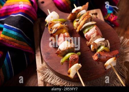 Hausgemachte Spieße mit Fleisch und gegrilltem Gemüse, serviert auf einem rustikalen Holzbrett, auch bekannt als Brochetten, Chuzo oder Pincho. Stockfoto