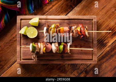 Hausgemachte Spieße mit Fleisch und gegrilltem Gemüse, serviert auf einem rustikalen Holzbrett, auch bekannt als Brochetten, Chuzo oder Pincho. Tabellenansicht. Stockfoto