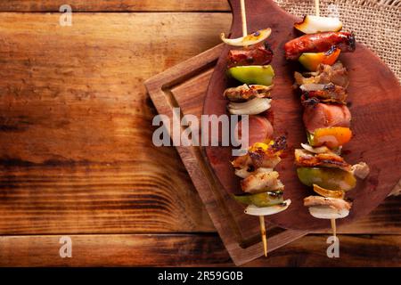 Hausgemachte Spieße mit Fleisch und gegrilltem Gemüse, serviert auf einem rustikalen Holzbrett, auch bekannt als Brochetten, Chuzo oder Pincho. Tabellenansicht. Stockfoto