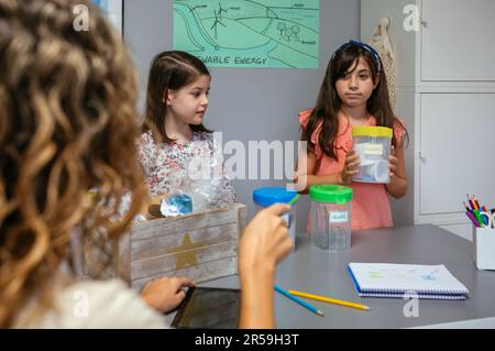 Schüler schaut auf Lehrer, während sie Mülltonnen in der Hand hält Stockfoto