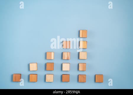 Leere Holzwürfel in Pyramidenfarben von dunkel bis hellbeige auf blauem Hintergrund. Minimalistische abstrakte Konzeptdarstellung des Fortschritts A. Stockfoto