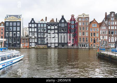 Die Tanzhäuser in Amsterdam. Farbenfrohe hohe Gebäude entlang des Kanals. Tanzende Häuser auf dem Damrak-Kanal. Bewölktes Wetter. Hochwertiges Foto Stockfoto