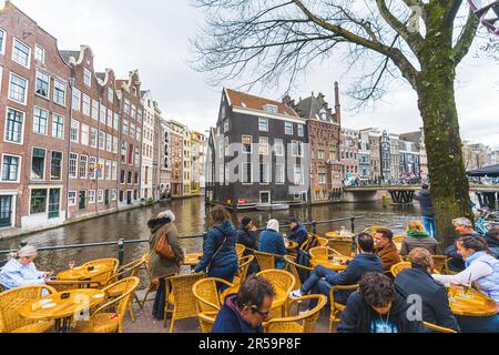 Touristen und Holländer genießen Kaffee am Ufer des Amsterdamer Kanals. Klassische Gebäude und Architektur. Hochwertiges Foto Stockfoto