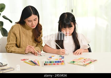 Kleines asiatisches Mädchen malt mit ihrer Mutter im Wohnzimmer. Familienheim Freizeitkonzept Stockfoto