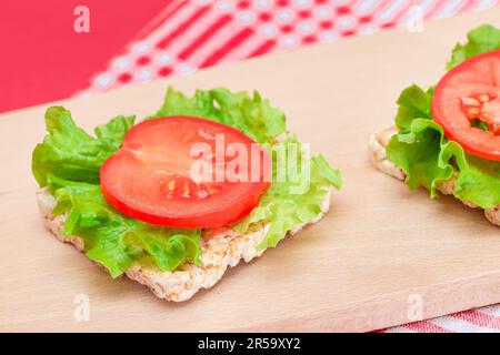 Reiskuchen-Sandwiches mit Tomaten und Salat auf Holzbrett. Einfaches Frühstück. Diät-Essen. Schnelle und gesunde Sandwiches. Knäckebrot mit leckerer Füllung. Gesunder Ernährungs-Snack Stockfoto