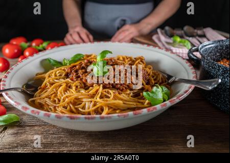 Frau, die eine große Nudelschüssel mit Spaghetti Bolognese auf rustikalem Holztisch hält oder serviert Stockfoto