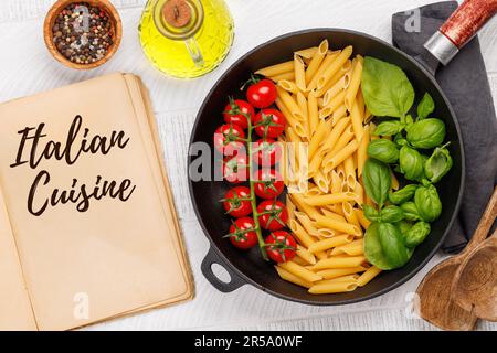 Eine lebendige Darstellung der italienischen Flagge mit Pasta, Basilikum und Tomaten, wunderschön präsentiert in einer Pfanne und einem Kochbuch. Flach verlegen mit Stockfoto