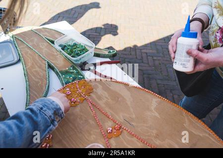 Mosaikkunstwerke aus recyceltem Kunststoff, Glas und anderen Materialien. Zwei Personen schmücken hölzerne Ausschnittbretter mit Pailletten. . Hochwertiges Foto Stockfoto