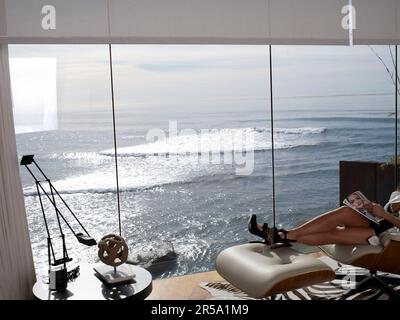 Eine Dame sitzt in einem Stuhl und liest in einem Haus am Meer in La Jolla, Kalifornien. Stockfoto