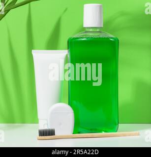 Erfrischende Mundspülung in einer durchsichtigen Plastikflasche und Zahnseide auf grünem Hintergrund Stockfoto