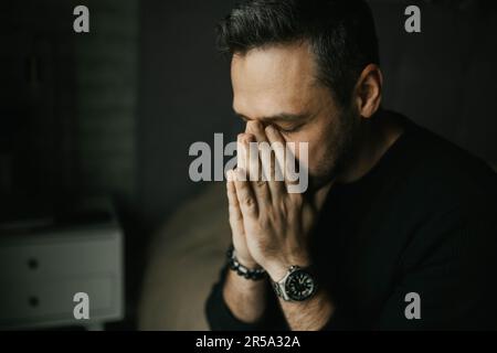 Ein trauriger Mann legte seine Hände ins Gesicht, als er auf dem Bett saß Stockfoto