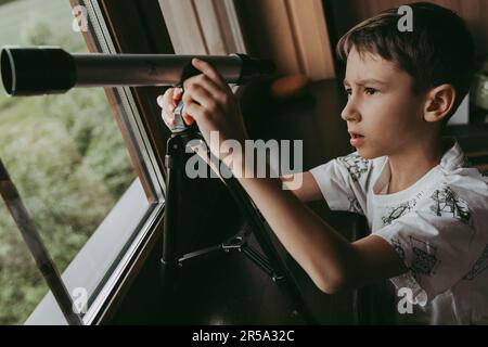 Der Junge schaut durch das Fenster auf das Teleskop Stockfoto
