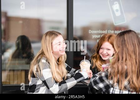 Drei glückliche Teenager-Mädchen, die vor einem Café was trinken. Stockfoto