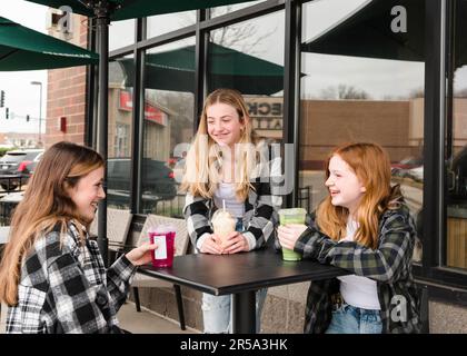 Drei glückliche Teenager-Mädchen, die vor einem Café was trinken. Stockfoto