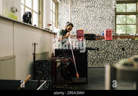 Künstlerischer kreativer Glasbläser, der in einem Studio arbeitet Stockfoto