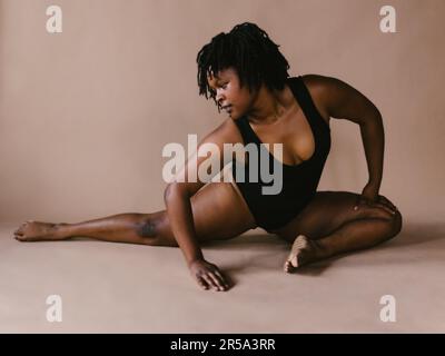 Schwarze Tänzerin in halbgeteilter Stretchtanz-Pose im Studio Stockfoto