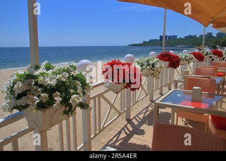 Das Foto wurde in der Stadt Odessa in der Ukraine aufgenommen. Das Bild zeigt ein gemütliches Café mit weißen und roten Blumen am Schwarzen Meer. Stockfoto